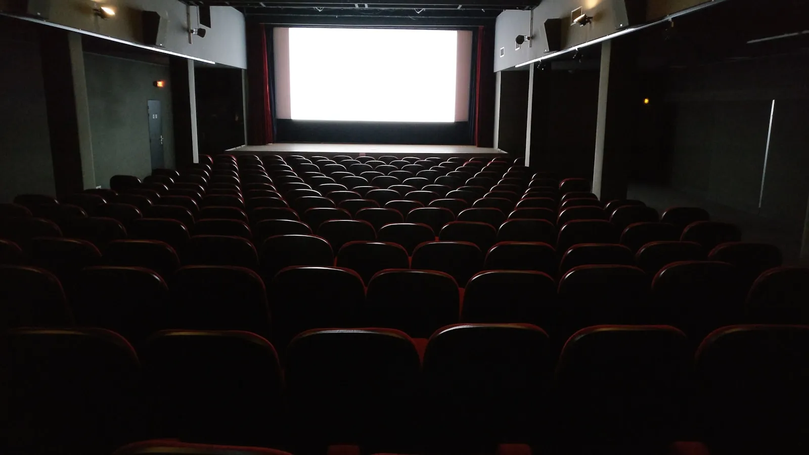A cinema auditorium in France with rows of seats facing a lit screen