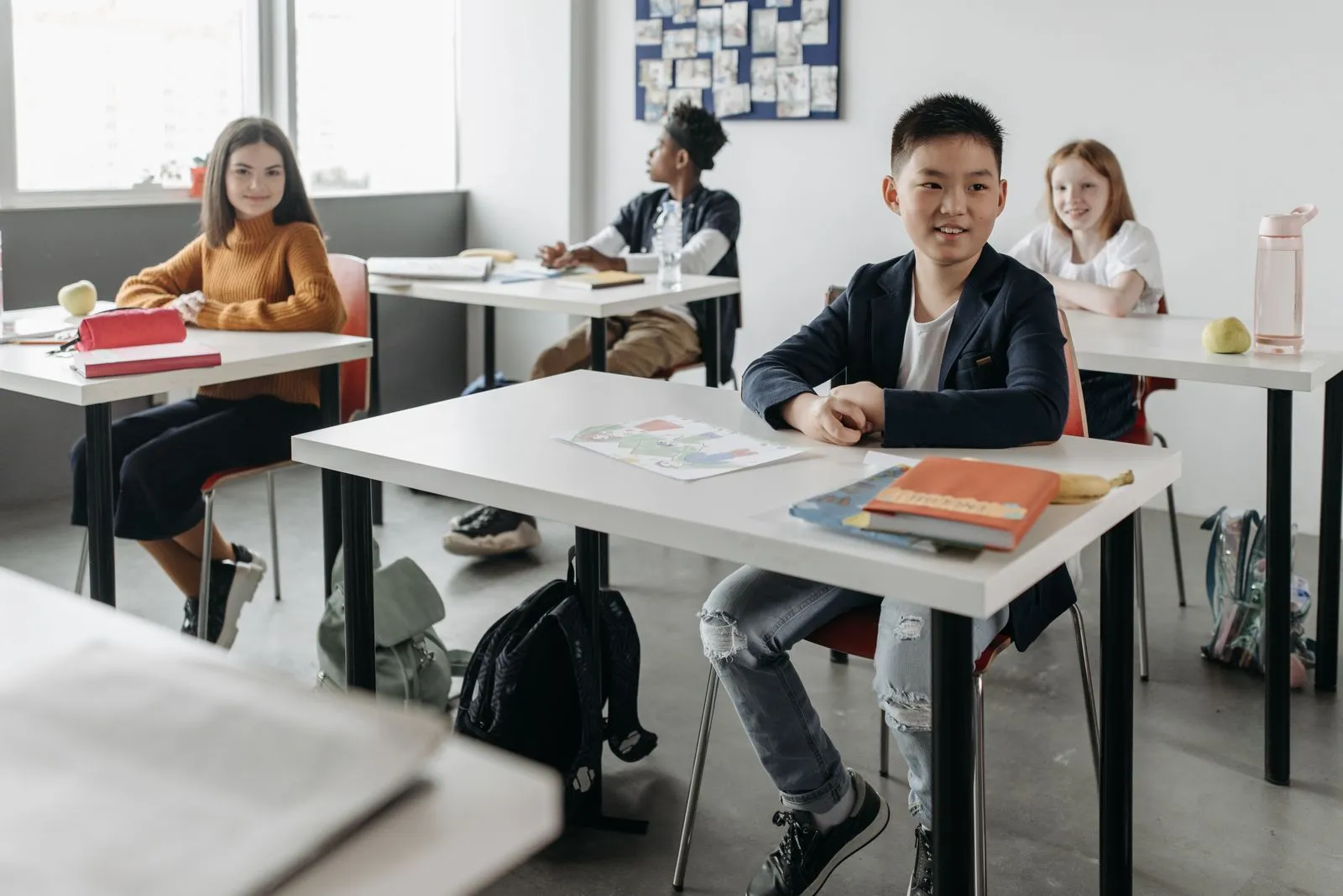 Four smiling international students of different backgrounds sitting at desks in a bright modern classroom