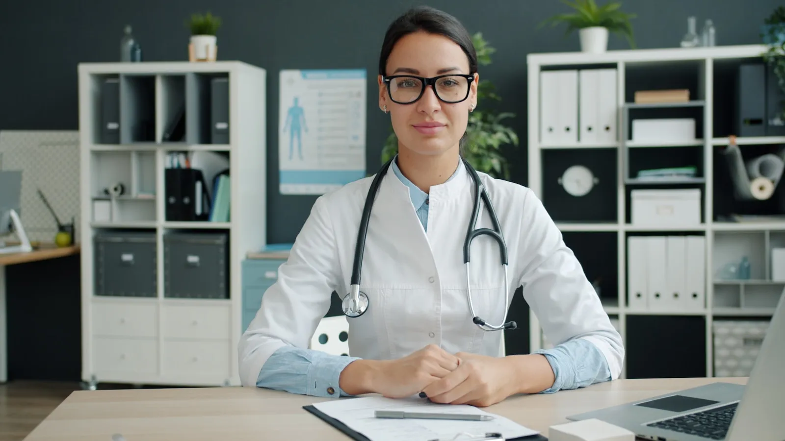 A smiling female doctor with a stethoscope sitting at her desk in a bright medical office