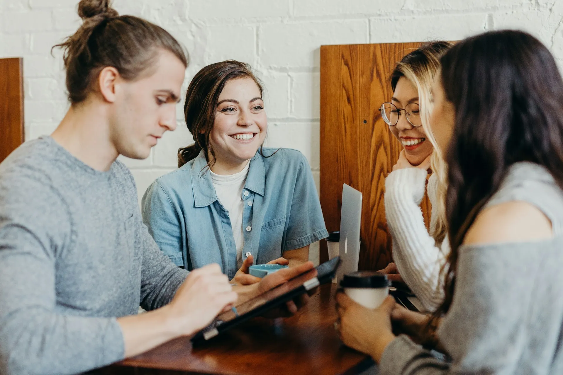 A group of friends chatting and smiling together around a table with laptops and coffee