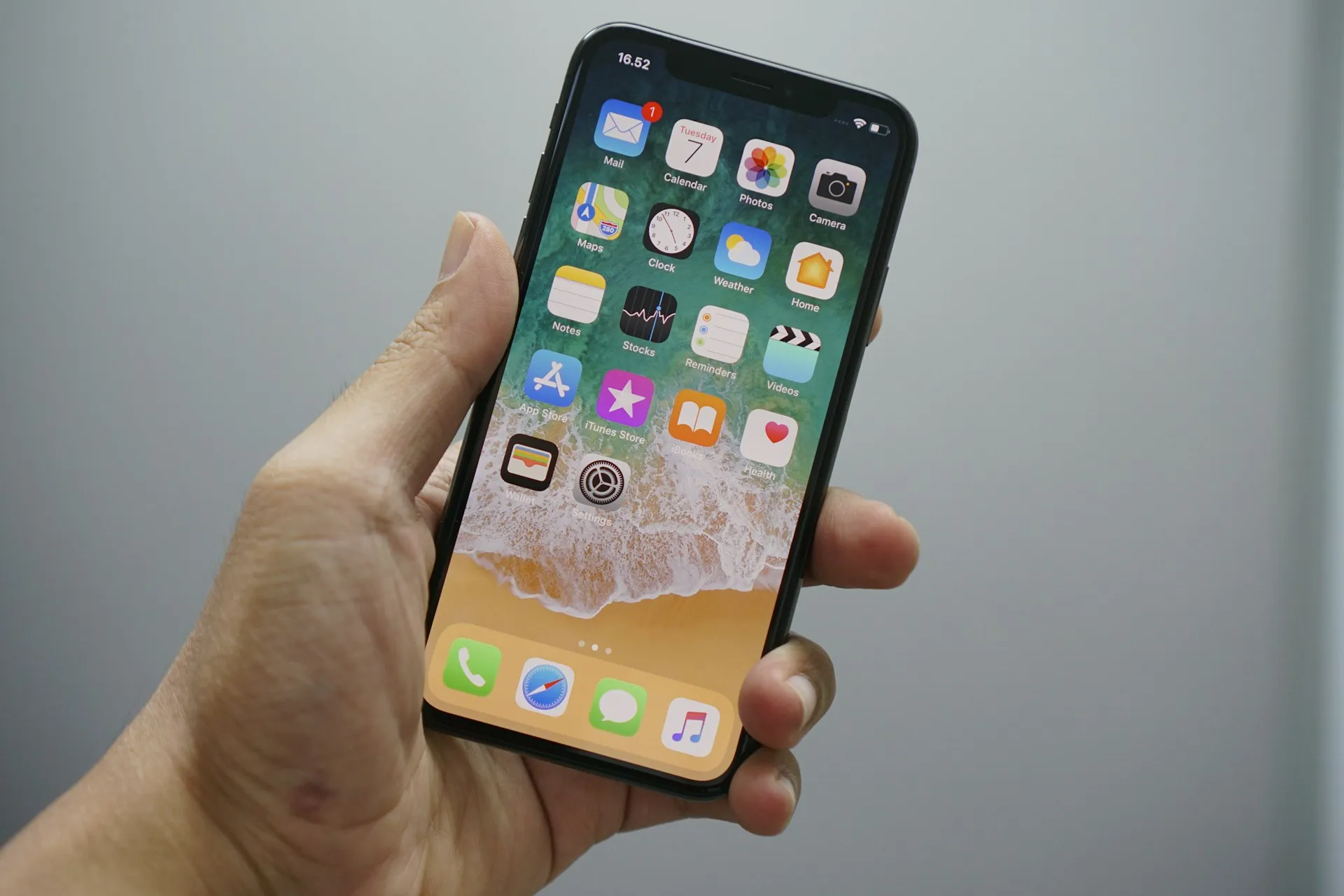 A hand holding an iPhone showing its home screen, against a plain gray background
