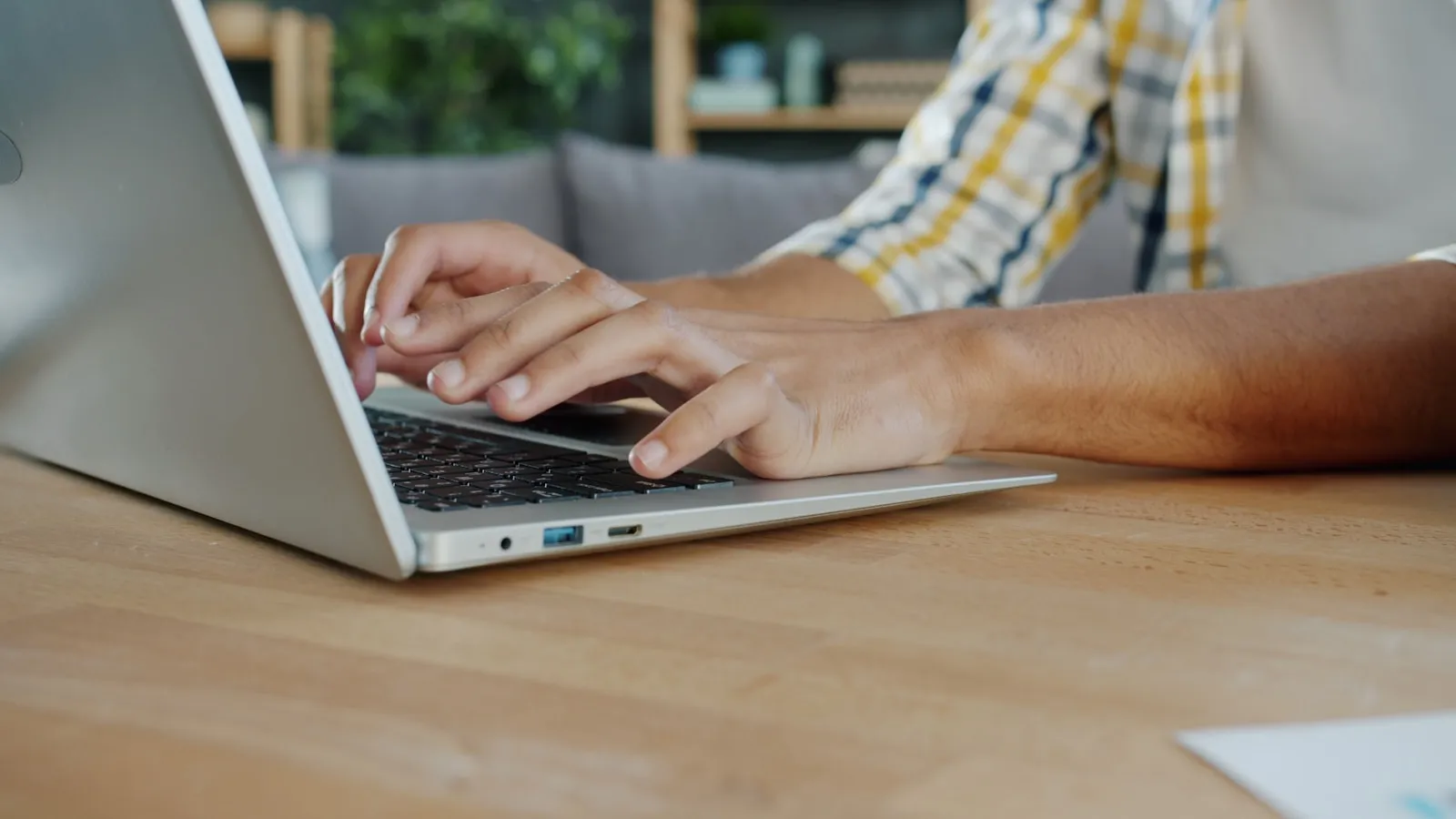 Close-up of hands typing on a laptop keyboard at a home desk