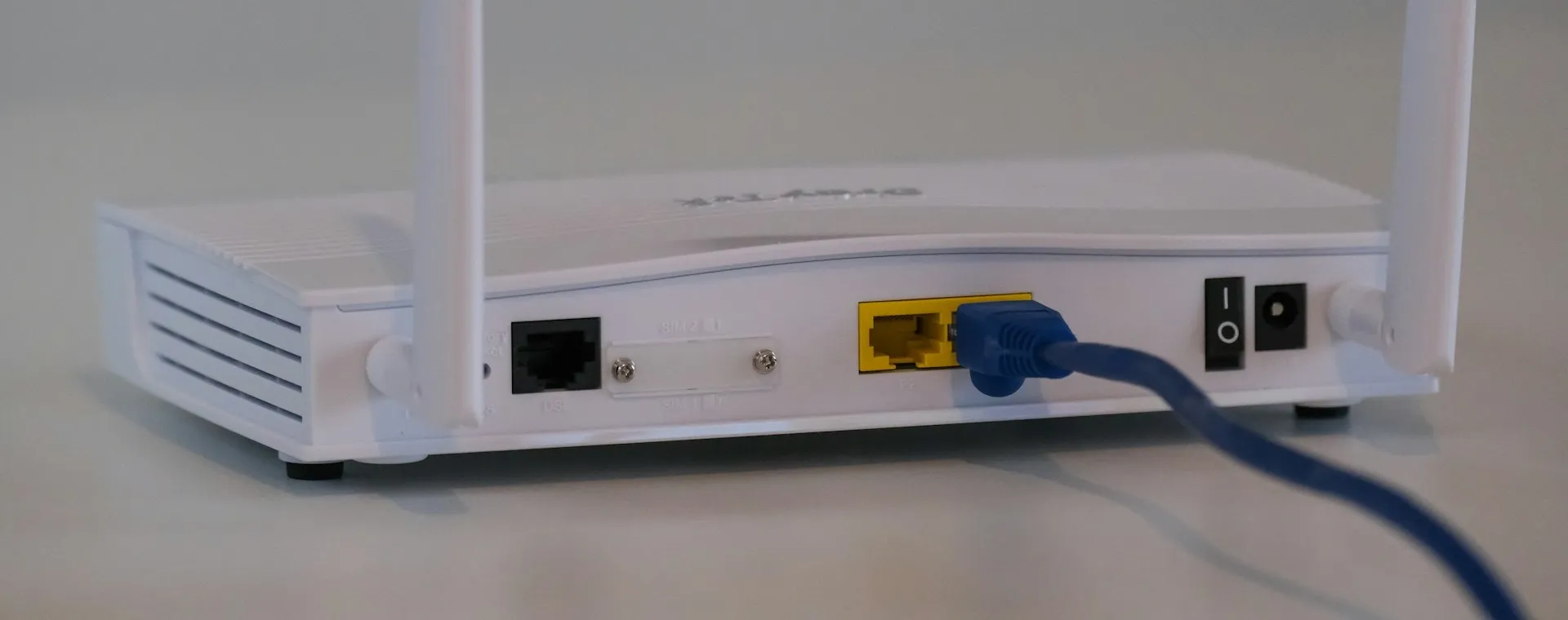 The back of a white home internet router with two antennas and a blue network cable plugged in