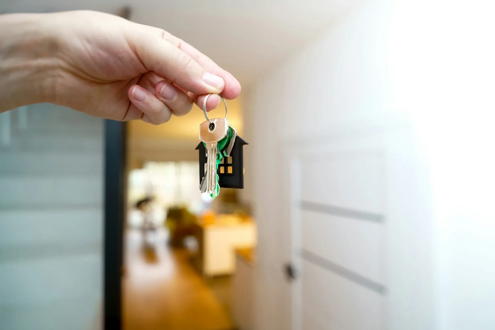 A hand holding a bunch of house keys with a house-shaped keychain in front of an open door