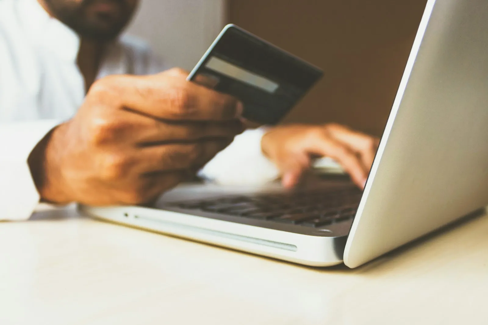 A person holding a bank card while typing on a laptop keyboard