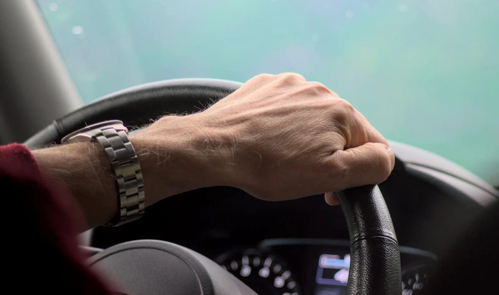 A hand gripping a car steering wheel while driving
