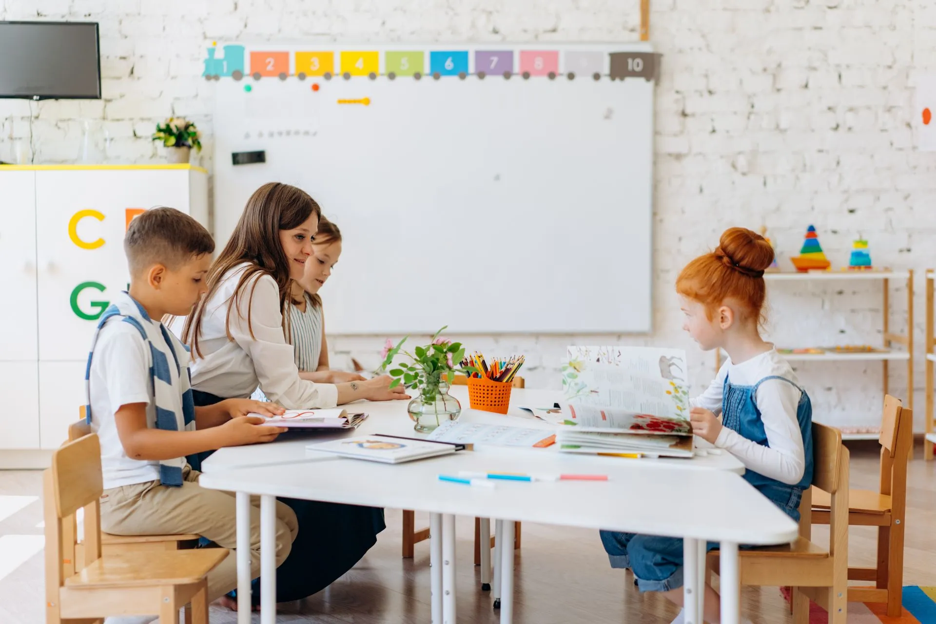 A teacher reading with young children at a table in a bright, colourful classroom