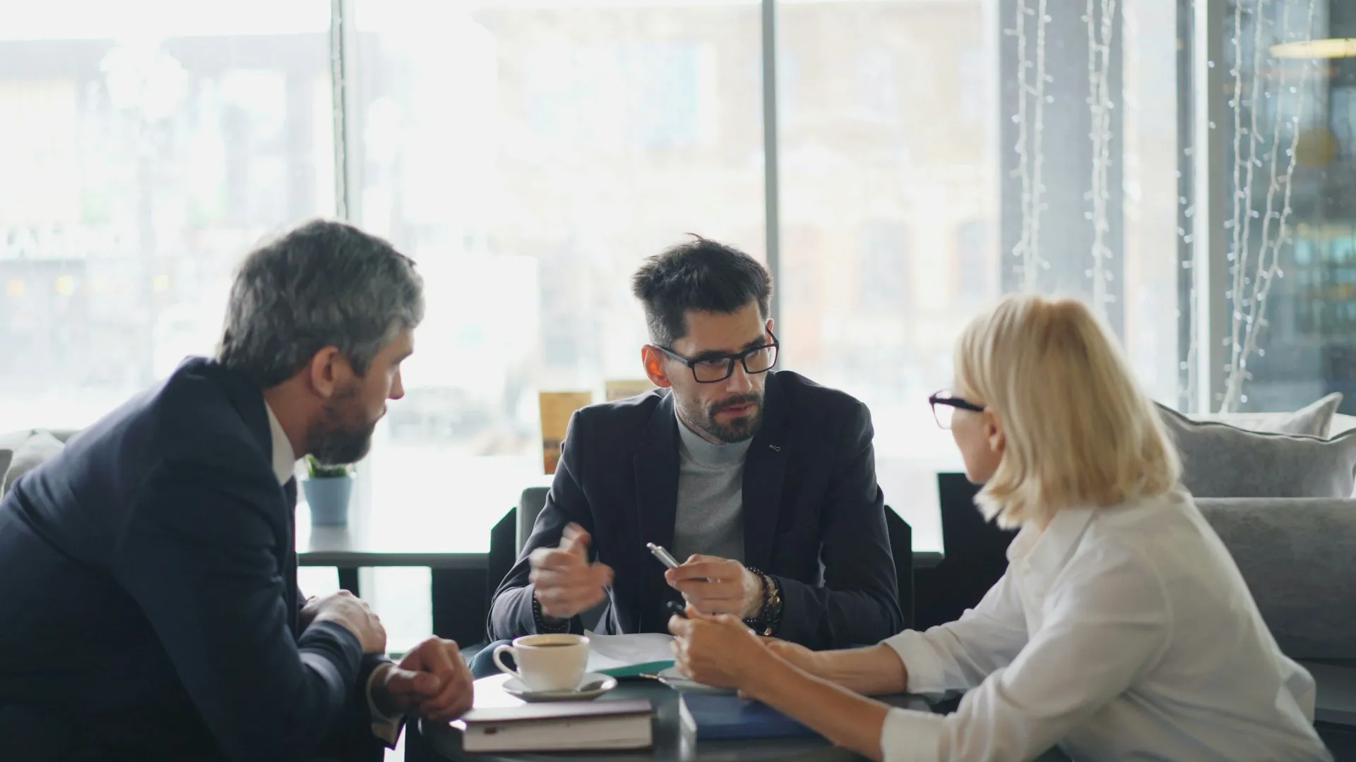 Three people in a meeting discussing documents over coffee at a table