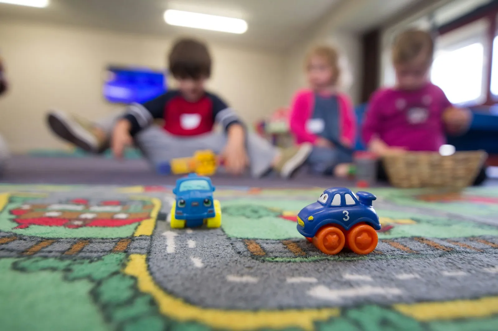Toy cars on a play mat with children playing in the background at a nursery